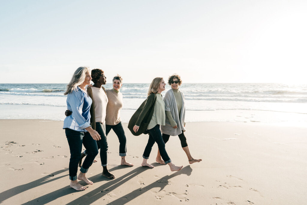 A group of bare-footed women stroll down the beach together.