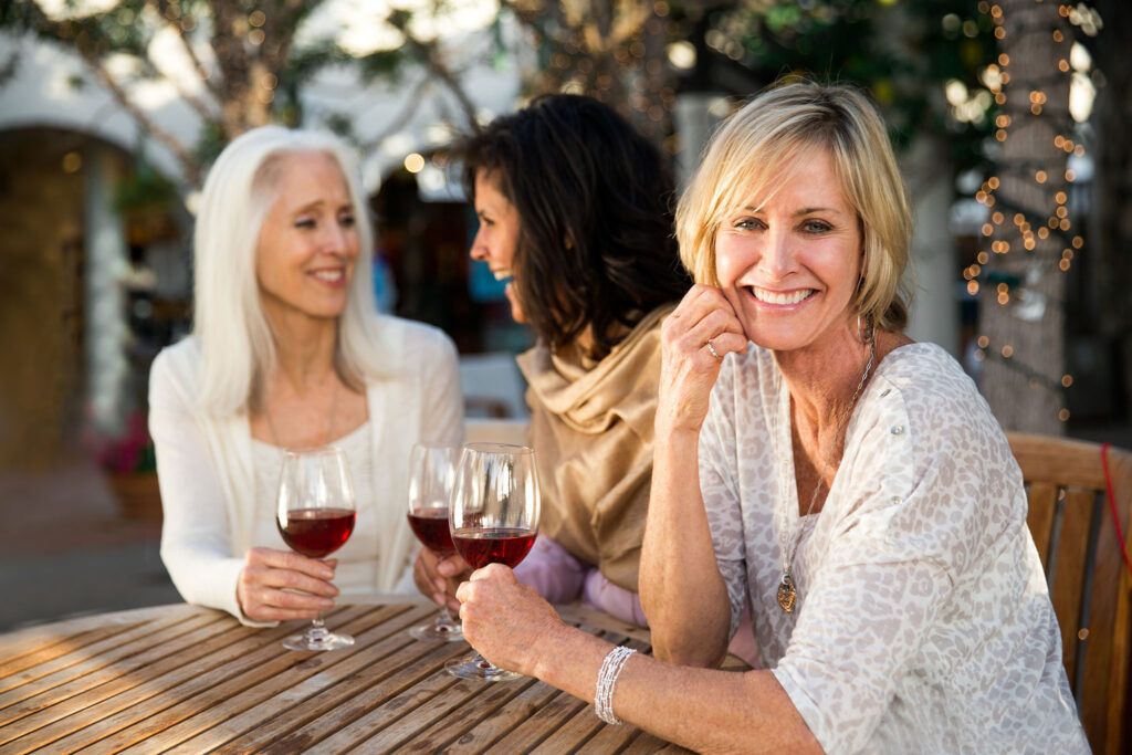 Three women enjoy wine around a wooden table.