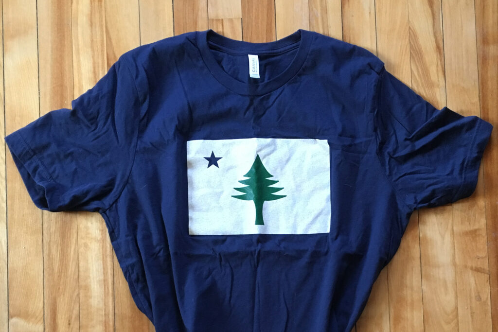 Camisa t-shirt com bandeira original de Maine, um pinheiro verde-escuro e estrela do norte azul.