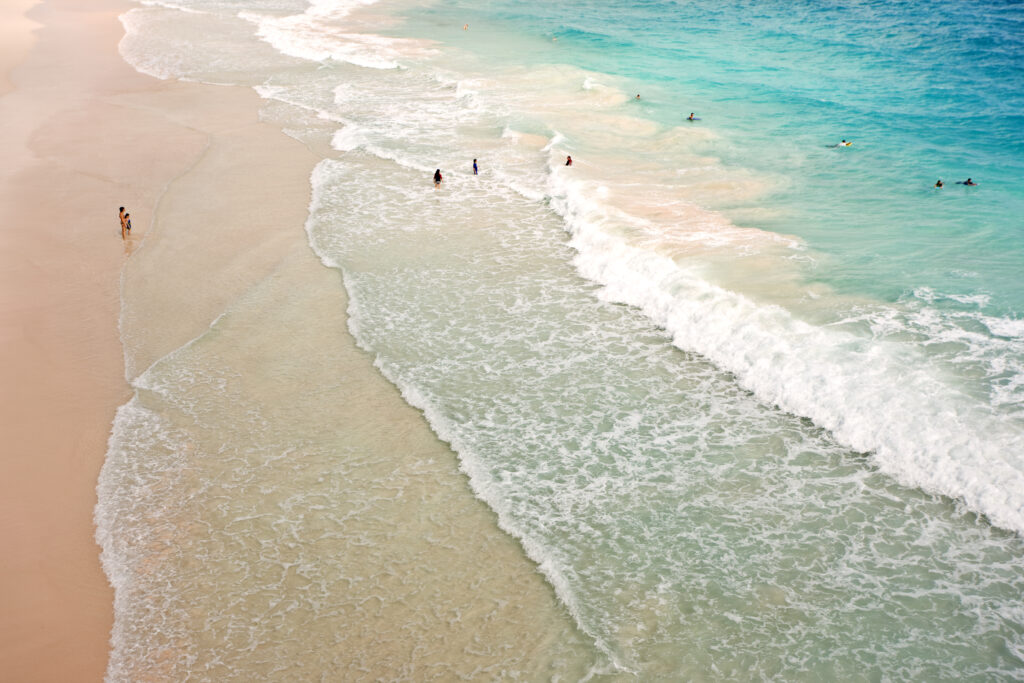 Swimmers paddling in the surf beside the pink sand of Crane Beach in Barbados.