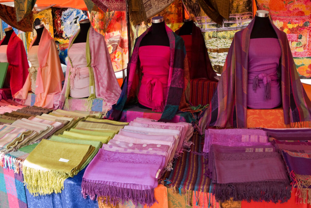 Colorful scarves, rugs, and cloths in an open market booth.