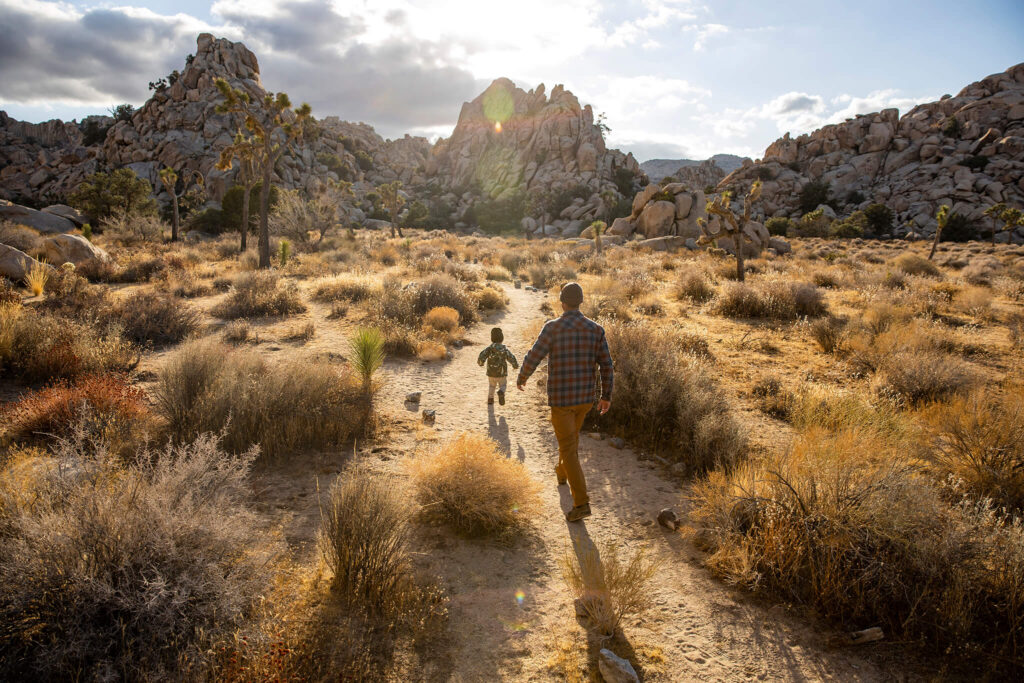 Father and son hike through desert brush to inspect a jumble of boulders.