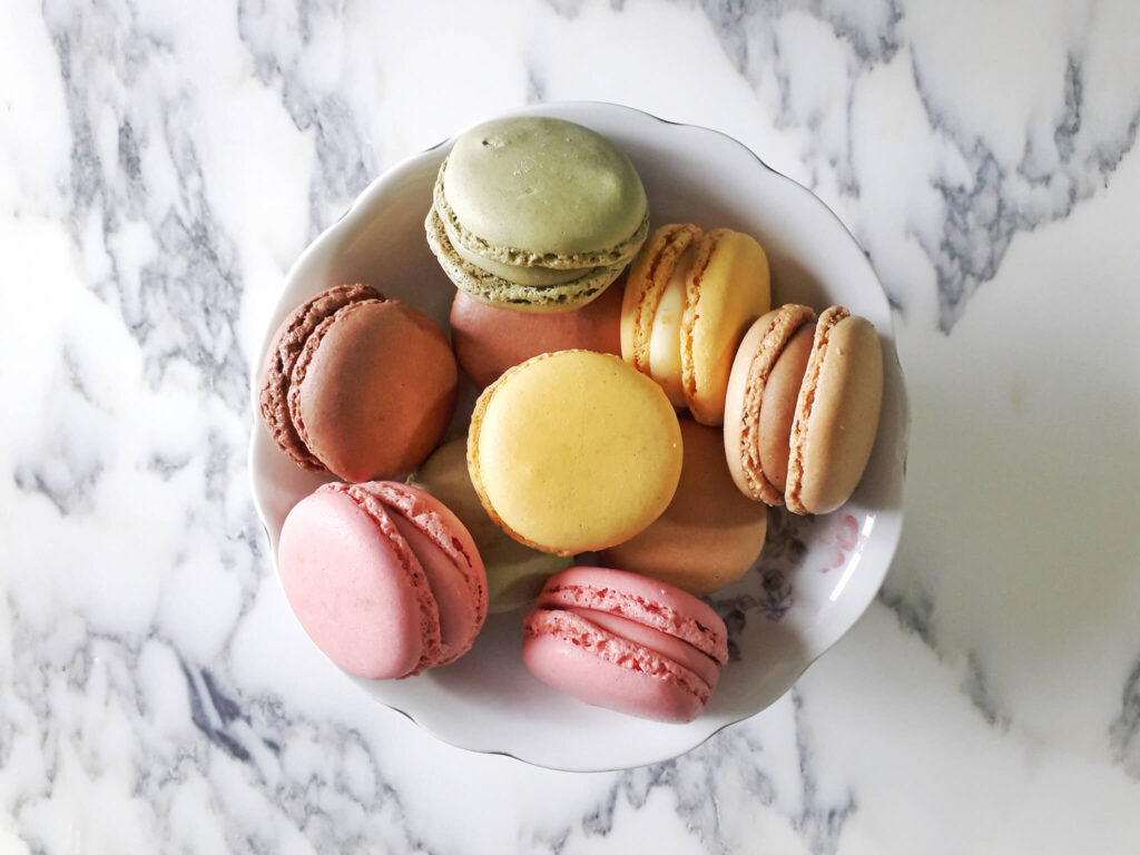 A bowl of French macarons sits on a marble table.