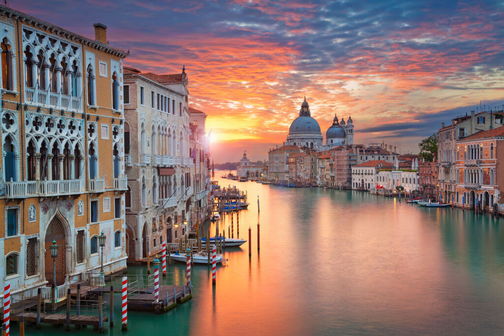 The setting sun reflects light off the calm water of a Venice canal.