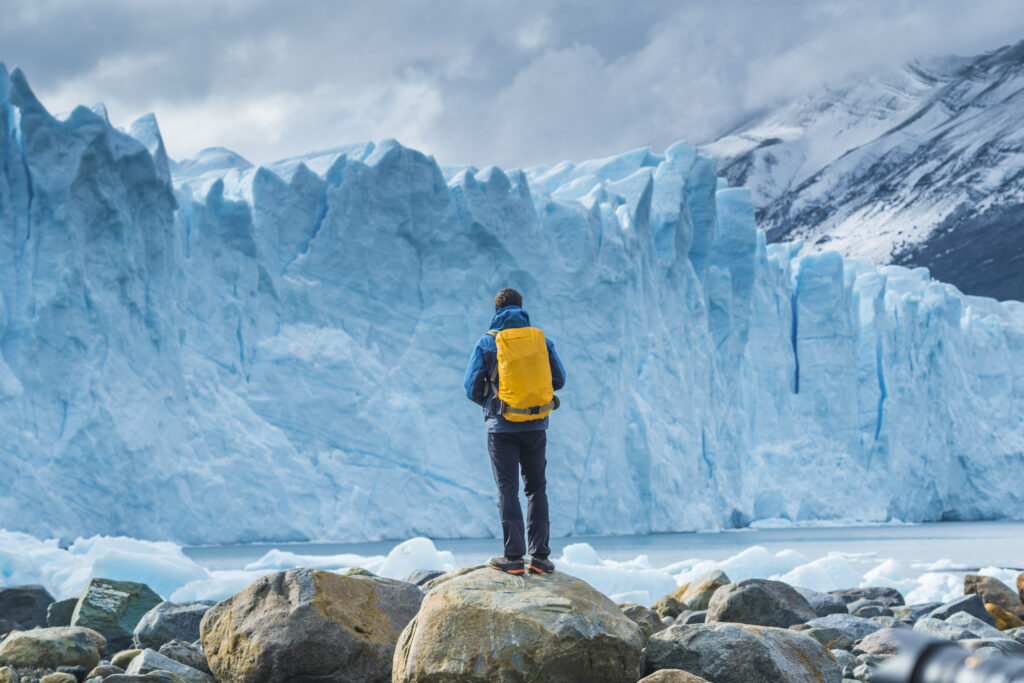Ein Tourist mit einem gelben Rucksack bewundert das bläulich schimmernde Eis des Perito-Moreno-Gletschers.
