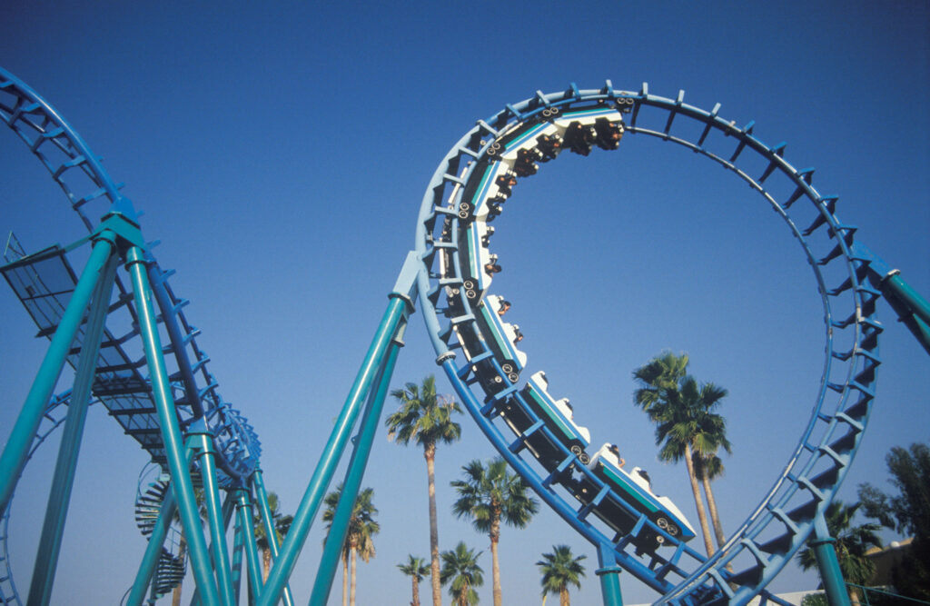 A roller coaster does a loop, surrounded by palm trees.